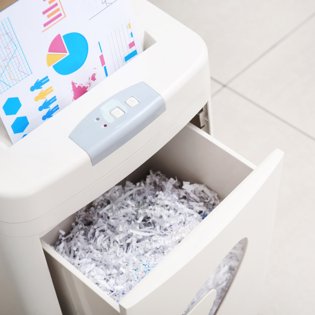A paper being fed into a shredder and the drawer of shedder opened - showing paper shredded